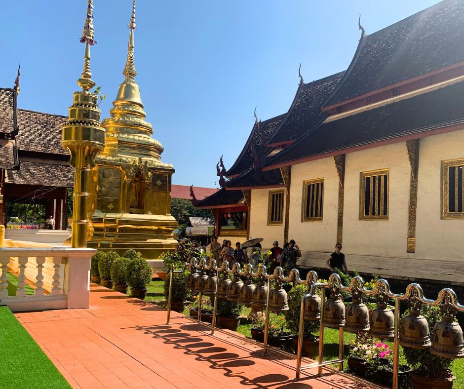 Exterior del Wat Phra Singh con pared blanca, techo oscuro y campanas